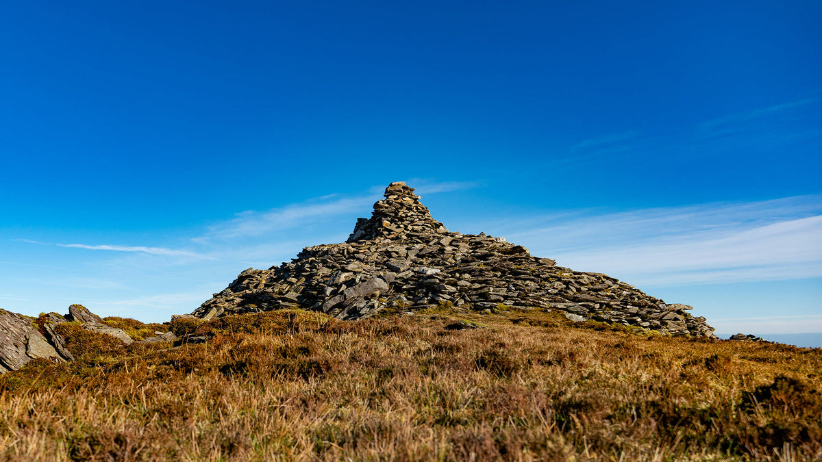 A stone cairn on a grassy hilltop under a blue sky