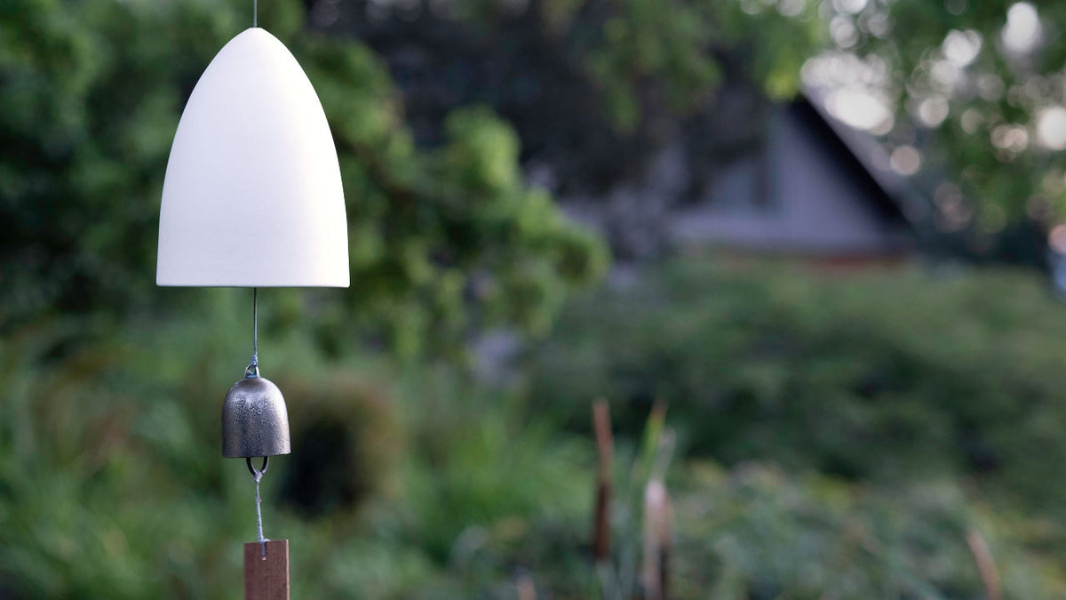 A white porcelain memorial wind chime with a bronze bell hanging in a garden